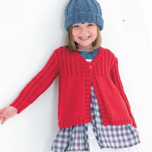 May include: A young girl wearing a red knitted cardigan with a button fastening, a blue and white checked dress, and a blue knitted hat with a pom-pom.