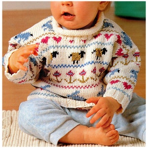May include: A white knitted baby sweater with a colourful pattern of animals, hearts, and anchors. The sweater has a high neck and long sleeves.