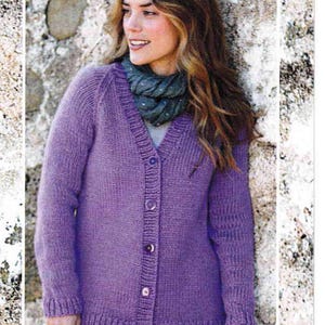 May include: A purple knitted cardigan with a V-neck and button closure. The cardigan has long sleeves and a relaxed fit. The model is wearing the cardigan with blue jeans and a gray scarf.