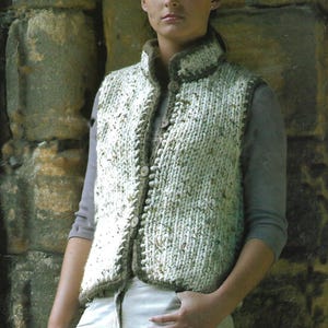 Könnte beinhalten: Eine weiße und braune Strickweste mit Knopfleiste. Die Weste hat einen hohen Kragen und ein strukturiertes Muster.