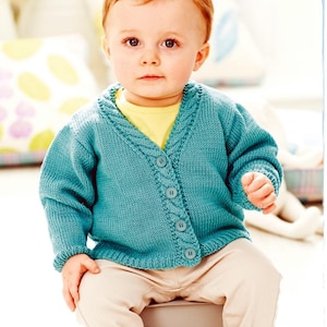 May include: A baby in a teal blue knitted cardigan with a cable knit design around the collar and button closure. The baby is also wearing a yellow top and beige trousers. The cardigan has long sleeves and ribbed cuffs.