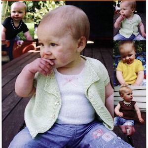 May include: A young child wearing a light green knitted cardigan with a white tank top underneath. The cardigan has a button closure and a collar. The child is wearing blue jeans with embroidered flowers.