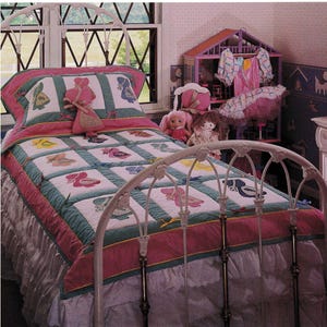 May include: A white metal bed frame with a floral design, dressed with a quilt and pillow set. The quilt features a patchwork design with ballet shoe motifs in various colours. The bed is decorated in a pink and green colour scheme, with a ruffled bed skirt.
