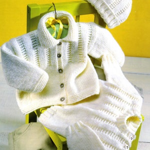 Könnte beinhalten: Ein weißes gestricktes Baby-Outfit-Set bestehend aus einem Cardigan, einer Hose und einer Mütze mit Bommel.