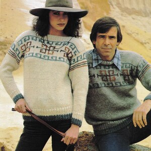 May include: Two people wearing matching knitted sweaters with geometric patterns. The woman wears a cream-colored sweater with blue, brown, and teal accents, paired with a wide-brimmed hat and dark pants. The man wears a gray sweater with similar patterns and blue jeans.
