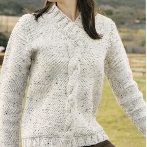 May include: A white knitted sweater with a cable knit design and a V-neck. The sweater has a speckled pattern throughout.