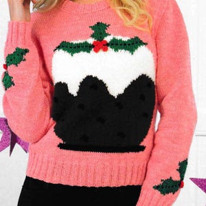 May include: Pink knitted jumper with a black and white Christmas pudding design. The jumper has green holly accents on the sleeves.