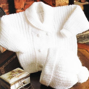 Puede incluir: Un cárdigan blanco de punto para bebé con cuello y cierre de botones, combinado con un gorro blanco de punto a juego con un pompón.