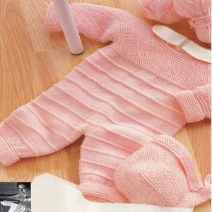 May include: A pink knitted baby outfit with a matching hat. The outfit has a ribbed texture and is made with soft yarn.