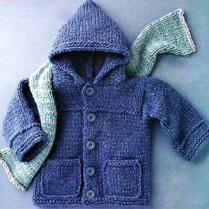 May include: A blue knitted hooded jacket with a matching scarf. The jacket has a button-up front, two front pockets, and a hood. The scarf is blue, white, and teal striped. The jacket is approximately 30 cm long.