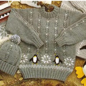 May include: A grey knitted jumper with a cable knit pattern and penguin designs. The jumper has a white snowflake pattern and a white trim around the neckline, cuffs, and hem.