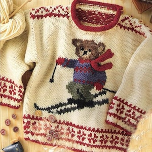 May include: Cream-colored knitted sweater featuring a teddy bear skiing design. The sweater has red and white patterned cuffs, hem, and neckline. The teddy bear wears a red scarf and a blue and purple sweater. Wooden buttons are on the shoulder.