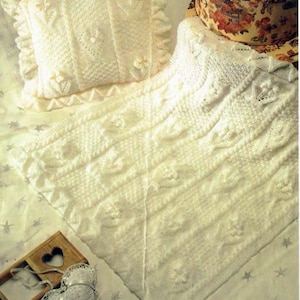 May include: A white knitted baby blanket with a delicate cable pattern and a matching pillow. The blanket is made with a soft yarn and has a delicate, lacy edge.