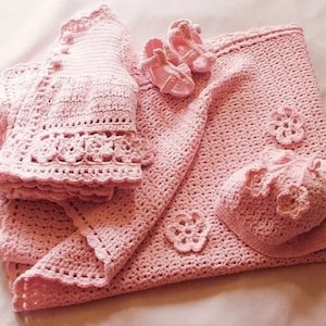 May include: A pink crocheted baby set including a blanket, a cardigan, a hat, and a pair of booties.