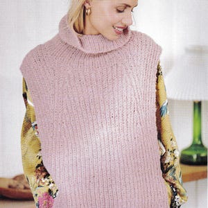 May include: A sleeveless, light pink knitted sweater with a turtleneck. The sweater has a ribbed texture and is worn over a yellow floral patterned top. The model is smiling and wearing gold hoop earrings.