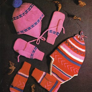 May include: A set of pink and red knitted winter accessories including a hat, mittens, and a neck warmer. The hat has a blue pompom on top and the mittens and neck warmer have a blue and white chevron pattern.