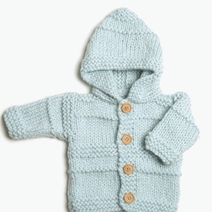 May include: A light blue knitted baby cardigan with a hood and wooden buttons.