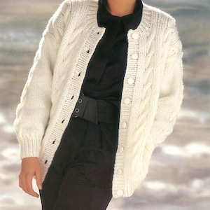 May include: A white cable knit cardigan with a button closure. The cardigan has a relaxed fit and is made of a soft, warm yarn.