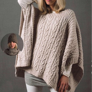 Könnte beinhalten: Ein beiger Strickponcho mit einem Zopfmuster. Der Poncho hat einen weiten Ausschnitt und eine lockere Passform. Er wird von einem Model mit einem weißen Shirt darunter getragen.