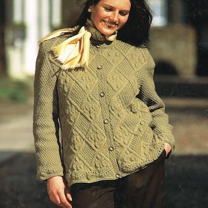 Könnte beinhalten: Ein grüner Strickcardigan mit einem Zopfmuster und Knöpfen. Der Cardigan hat eine lockere Passform und wird von einer Person mit langen braunen Haaren getragen.