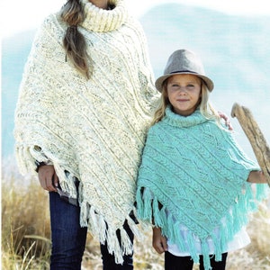 Puede incluir: Dos personas llevando ponchos de punto con flecos. El adulto lleva un poncho blanco y el niño lleva un poncho turquesa. Ambos ponchos tienen un patrón de punto de cable.