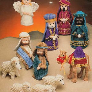 May include: A collection of crocheted Christmas nativity figures, including an angel, three wise men, Joseph, Mary, a camel, and several sheep. The figures are in various colors, including white, blue, purple, and brown. The angel has white wings.