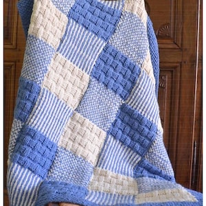 Könnte beinhalten: Eine blaue und weiße gestrickte Babydecke mit Patchwork-Muster. Die Decke ist mit verschiedenen Maschen gearbeitet, darunter Streifen und ein Korbgeflechtmuster.