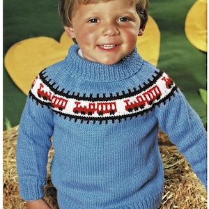 Könnte beinhalten: Ein blauer Strickpullover mit einem roten, weißen und schwarzen Muster am Halsausschnitt, das ein Zugmotiv zeigt. Der Pullover hat einen Rollkragen.