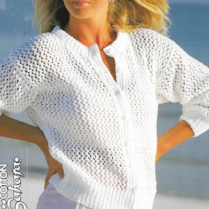 May include: A white, open-weave crochet cardigan with a button-up front. The long-sleeved sweater has a round neckline and is made of a textured, possibly cotton, material. The image also includes the text "Cotton Saharajas".