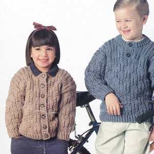 May include: Two children wearing knitted sweaters. The girl is wearing a brown sweater with buttons and a red and green bow in her hair. The boy is wearing a blue sweater with buttons.