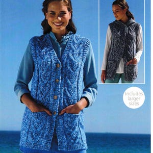 Könnte beinhalten: Eine blaue und weiße Strickweste mit Kabelmuster, Taschen und Knöpfen. Die Weste ist lang und hat einen V-Ausschnitt. Das Model trägt ein blaues Jeanshemd und einen blauen Jeansrock. Der Text "Enthält größere Größen" ist im Bild sichtbar.