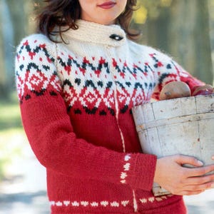 May include: A red, white, and black patterned knit cardigan with a cream-colored collar. The cardigan has a button closure and is worn by a person holding a wooden bucket. The sleeves and lower portion of the cardigan are solid red.
