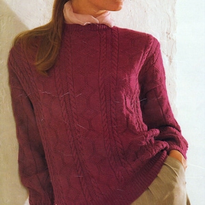 May include: A burgundy cable-knit sweater with a crew neck and long sleeves. The sweater is paired with tan pinstripe trousers and a brown hat with a bow. The outfit is completed with a light pink scarf.