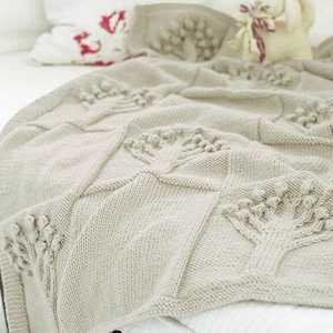 May include: A cream-colored knitted throw blanket with a repeating pattern of stylized trees. The blanket is made with a chunky yarn and has a soft, textured surface.
