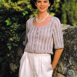 May include: A light purple knitted cardigan with a scoop neck and short sleeves. The cardigan has a button closure and a delicate lace pattern.