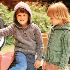 May include: Two children wearing knitted hooded sweaters. The boy is wearing a blue and brown sweater with a button closure. The girl is wearing a green sweater with a zipper closure.