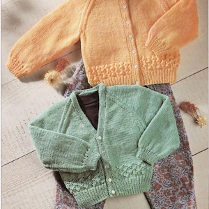 Puede incluir: Dos cárdigans de punto, uno de color naranja claro y el otro de color verde claro, ambos con cierre de botones. Los cárdigans están colocados sobre una superficie de madera con un pantalón estampado debajo.