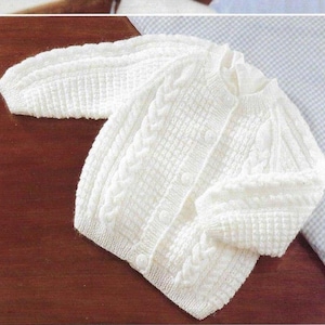 May include: White knitted baby cardigan with a cable knit pattern and button closure.