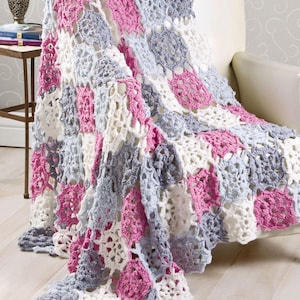 May include: A handmade crochet blanket draped over a chair. The blanket features a patchwork design with squares of white, light gray, and pink. The open weave pattern creates a delicate, textured appearance.