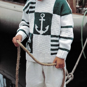 Op de afbeelding: Een wit en groene nautische trui met een ankerontwerp. De trui wordt gedragen met een witte korte broek. De persoon houdt een touw vast. De trui heeft groene accenten en een textuurpatroon.