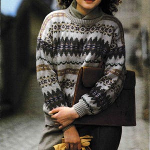 以下が含まれることがあります： 長袖のクリーム色、茶色、青の模様のセーターを着た女性。彼女は茶色の革のバッグを持っています。