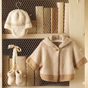 Peut inclure: Un bonnet en tricot texturé couleur crème avec des oreillettes, un gilet à capuche en tricot beige avec une fermeture à bouton unique et un ourlet marron clair, et une paire de chaussons en tricot crème liés par un ruban en satin.