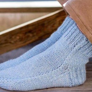 May include: A pair of light blue knitted socks with a textured pattern. The socks are being worn on someone's feet.