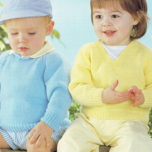 May include: Two children wearing knitted sweaters. One child is wearing a light blue sweater with a yellow collar and a blue and white striped hat. The other child is wearing a yellow V-neck sweater. Both sweaters have ribbed cuffs and hems.