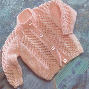 May include: A pale pink knitted baby cardigan with a button-up front and a delicate openwork pattern.
