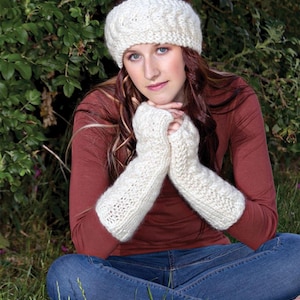 May include: A white knitted headband and matching fingerless gloves. The headband has a cable knit pattern and the gloves are long and loose fitting.