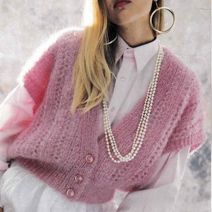 May include: A pale pink, open-knit cardigan with three buttons. The cardigan is worn over a light pink button-down shirt and white skirt. A layered pearl necklace and large gold hoop earrings complete the outfit.