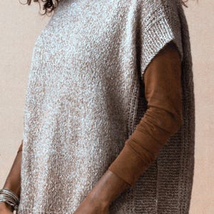 May include: A sleeveless knitted top in a light brown and white speckled pattern. The top has a high neckline and a relaxed fit.