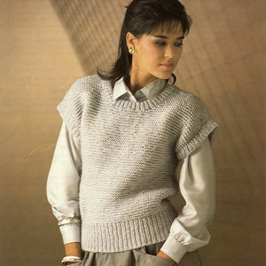 Puede incluir: Un jersey de punto gris claro sin mangas con cuello redondo. El jersey está hecho con un patrón de punto texturizado.