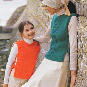 Puede incluir: Dos personas con chalecos de punto. Una persona lleva un chaleco naranja brillante con un diseño floral en los laterales. La otra persona lleva un chaleco verde azulado con un diseño de punto trenzado. Ambos llevan camisas de manga larga y faldas.